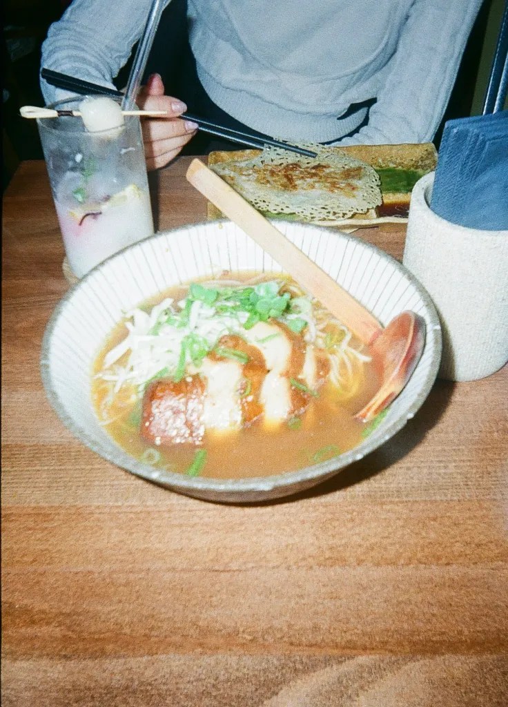 Vegan ramen in a bowl featuring mock meat, noodles, broth, and a wooden spoon.
