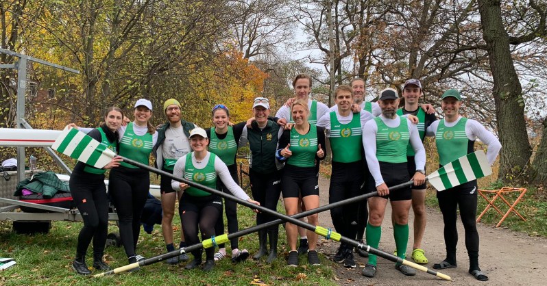 Julian poses with his Swedish rowing team, in all their gear holding two rowing paddles.