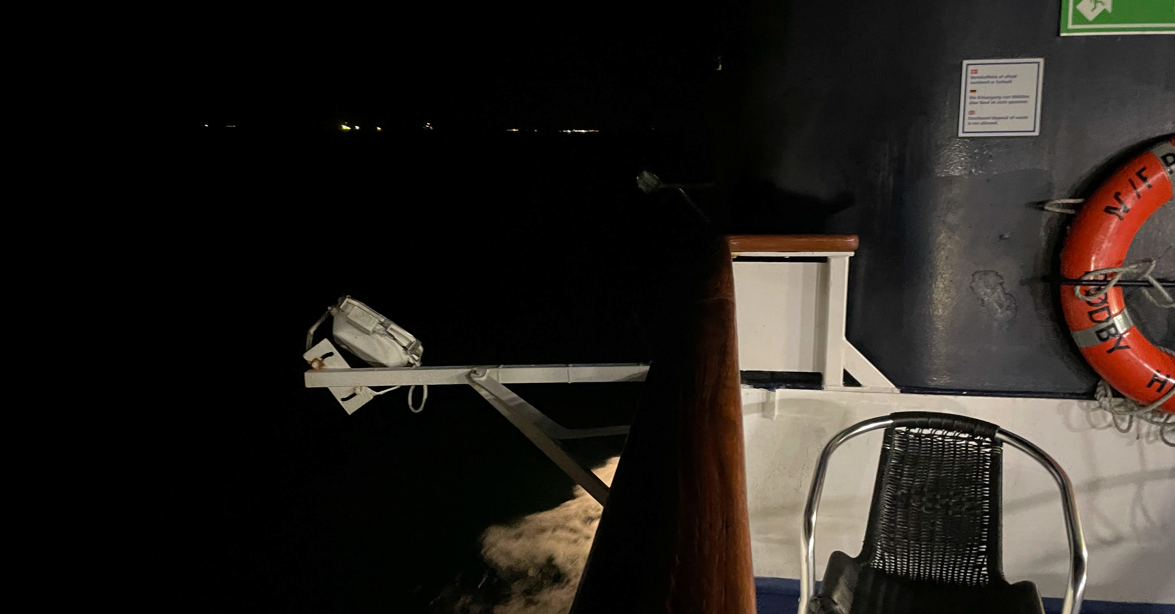 The railing of the ferry crossing the sea to Germany in the dark of night, with the ocean splashing against the side of the ship.