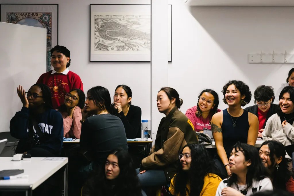 A group of 15 students sit and smile together at a Students of Color Affinity Group event.